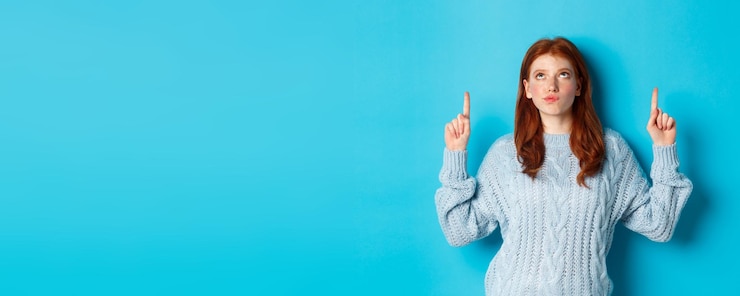 Free Photo winter holidays and people concept thoughtful redhead girl in sweater staring and pointing fingers u