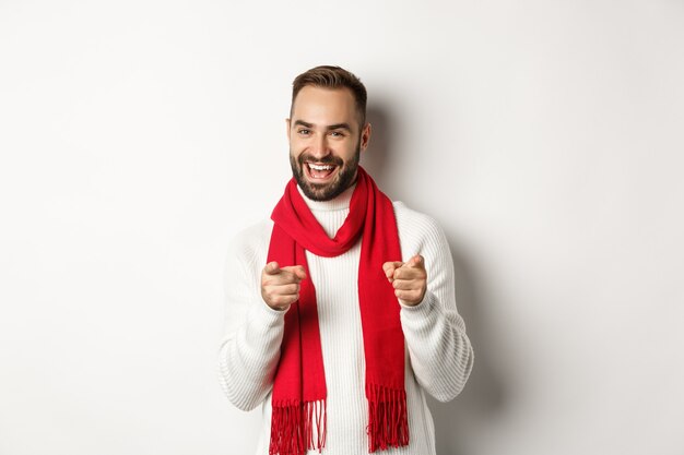 Winter holidays and shopping concept. Bearded man pointing fingers at you to praise or say congrats, wishing happy christmas, standing over white background