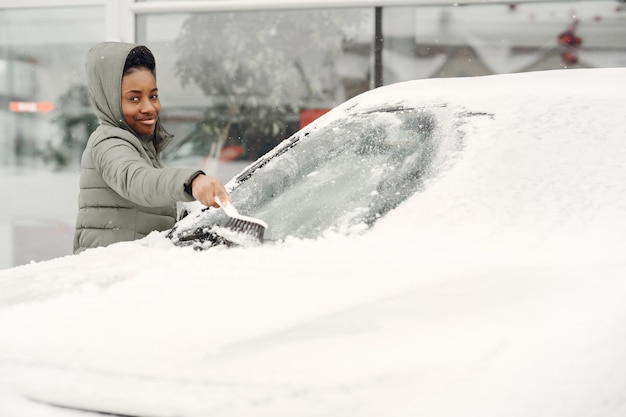 車から雪を掃除するアフリカの女性の冬の肖像画。緑のジャケットを着た女性。