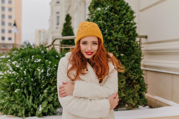 Winter portrait of shy ginger girl. Outdoor photo of european woman wears hat and coat.