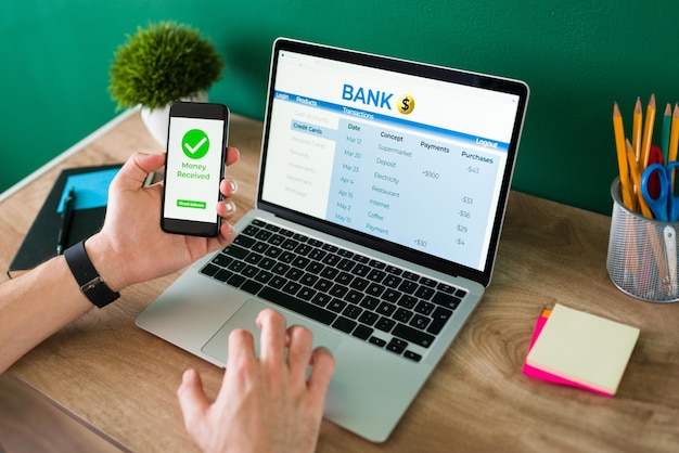 Wire transfer. Young man using his smartphone and laptop to do a banking transaction and some payments