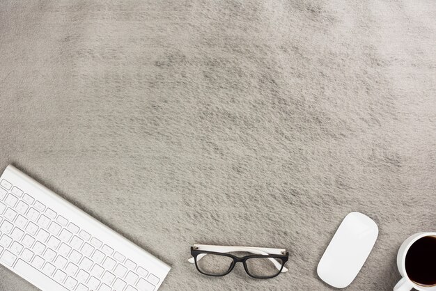 Wireless keyboard; mouse; eyeglasses and coffee cup on gray desk