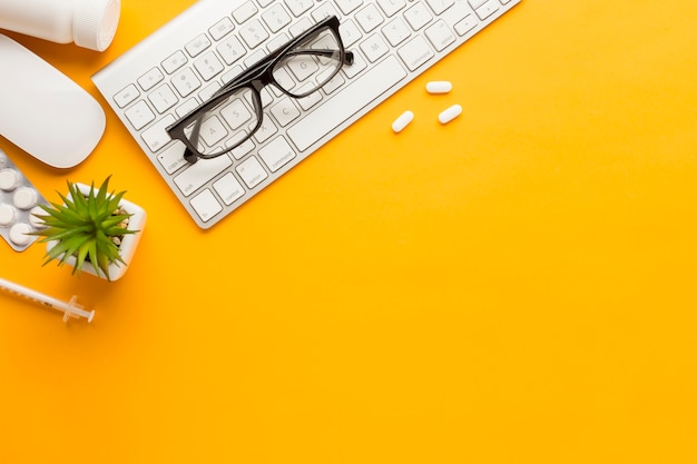 Wireless keyboard and mouse with tablets; succulent plant; eyeglasses against yellow surface