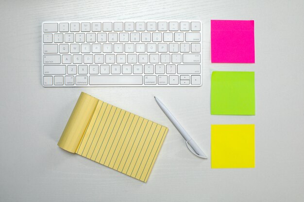 Wireless keyboard and yellow notepad and stick paper on the table