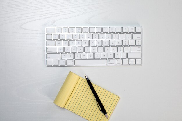 Беспроводная клавиатура и желтый блокнот на столе