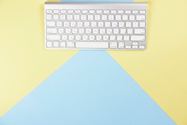 黄色と青の背景にワイヤレスの白いキーボード