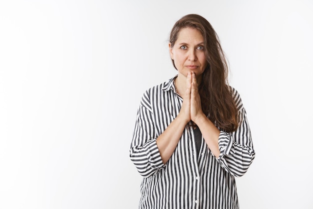 Wise and worried lady praying with palms pressed together over chest looking sincere, serious at camera