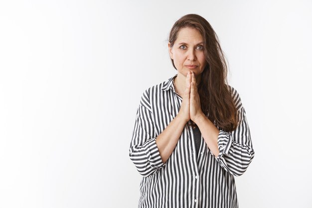 Wise and worried lady praying with palms pressed together over chest looking sincere, serious at camera