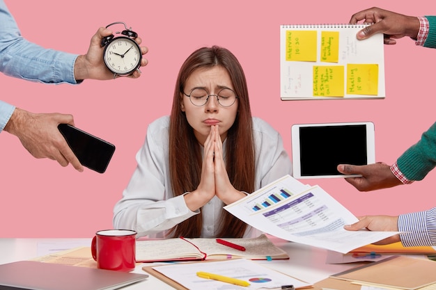 Foto gratuita desideroso studente universitario tiene le mani nel gesto di preghiera, crede nella buona fortuna, chiude gli occhi, prepara il compito in economia, chiede a dio che i sogni si avverino