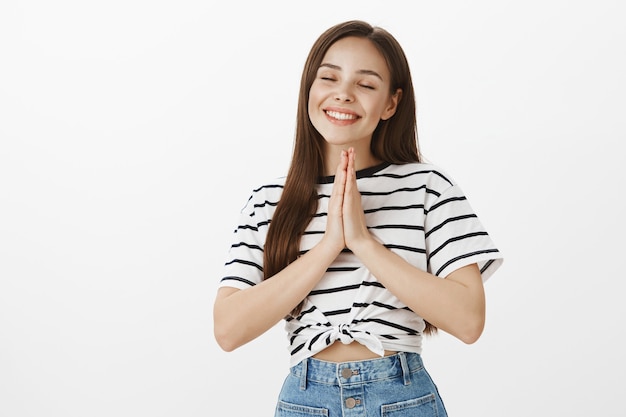 Wishful and hopeful attractive girl holding hands in plead while praying to god, begging