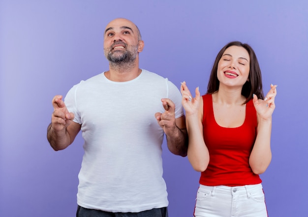 Wishing adult couple both doing crossed fingers gesture man looking up and woman with closed eyes 