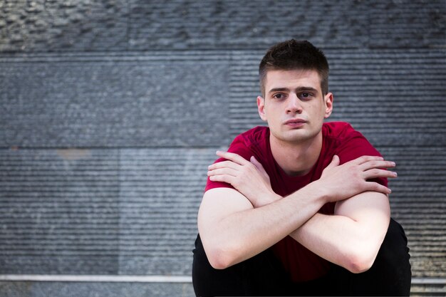 Wistful male teenager sitting on ground with arms crossed