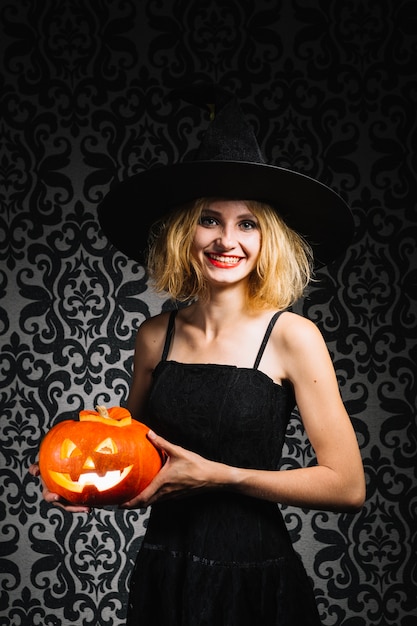 Witch girl smiling and holding pumpkin