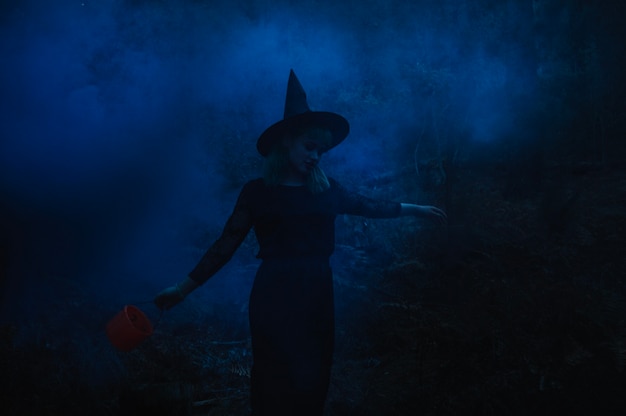 Free photo witch girl with bucket in night forest