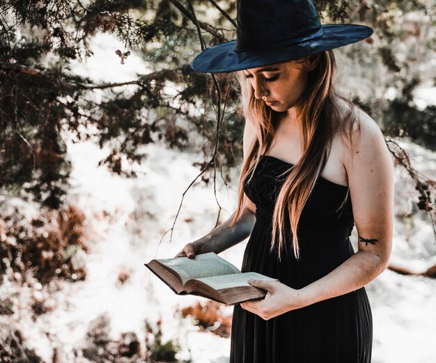 Witch in hat reading aged book in forest daytime