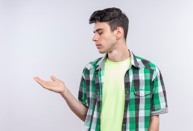 With closed eyes caucasian young guy wearing green shirt holding out hand to side on isolated white