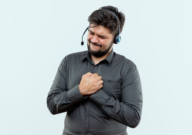 With closed eyes concerned young call center man wearing headset holding hands together isolated on white