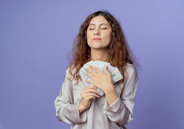 With closed eyes impressed young pretty girl holding money isolated on blue wall