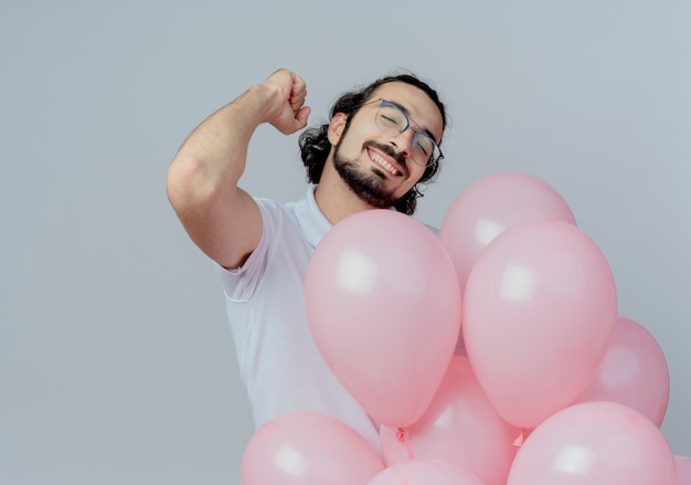 With closed eyes joyful handsome man wearing glasses holding balloons and showing yes gesture isolated on white