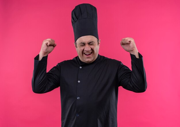 With closed eyes joyful middle-aged male cook in chef uniform showing yes gesture