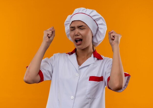 With closed eyes joyful young cook female wearing chef uniform showing yes gesture on isolated orange background