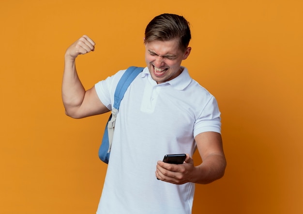 With closed eyes joyful young handsome male student wearing back bag holding phone