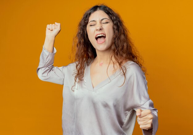 With closed eyes joyful young pretty girl raising fist isolated on yellow wall