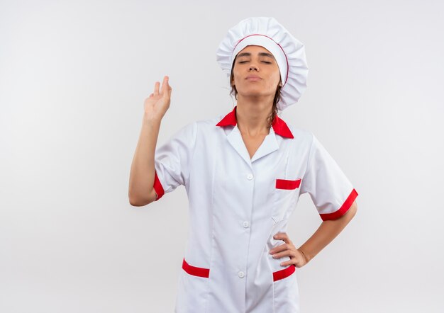 With closed eyes pleased young female cook wearing chef uniform showing okey gesture with copy space