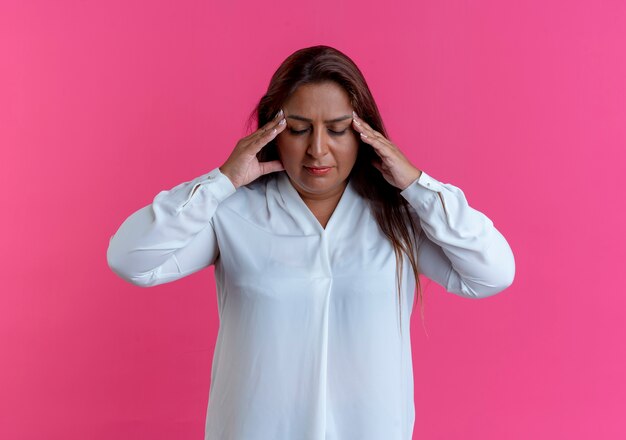 With closed eyes tired casual caucasian middle-aged woman putting hands on forehead isolated on pink wall