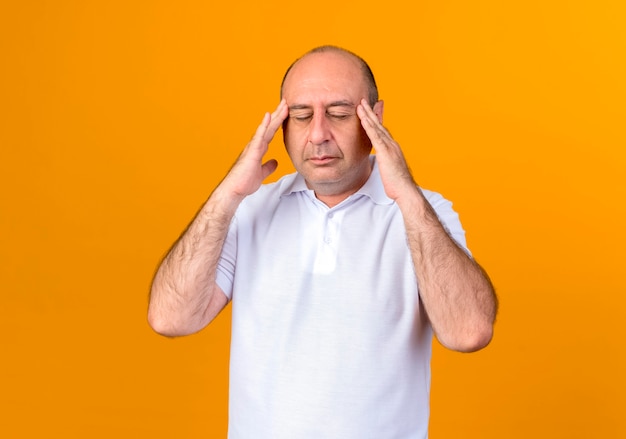 With closed eyes tired casual mature man putting hands on temple isolated on yellow wall