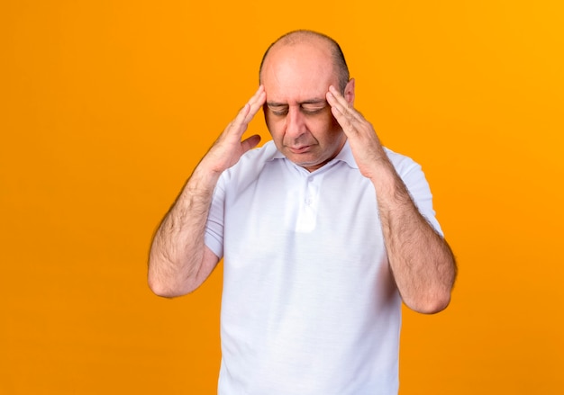 With closed eyes tired casual mature man putting hands on temple isolated on yellow wall