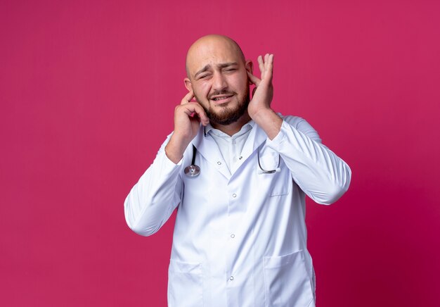 With closed eyes unpleased young male doctor wearing medical robe and stethoscope