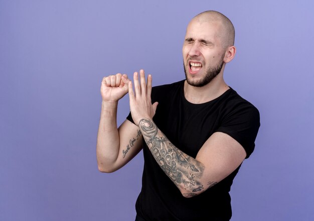 With closed eyes unpleased young sporty man showing different gestures isolated on purple