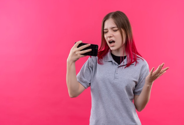 닫힌 된 눈으로 젊은 아름 다운 소녀 복사 공간이 격리 된 분홍색 벽에 전화를 들고 회색 티셔츠를 입고