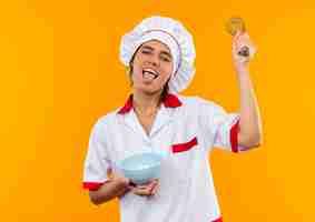 Free photo with closed eyes young female cook wearing chef uniform holding bowl and whisk showing tongue  with copy space
