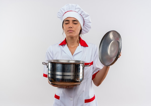 目を閉じて、コピースペースで鍋と蓋を保持しているシェフの制服を着た若い女性料理