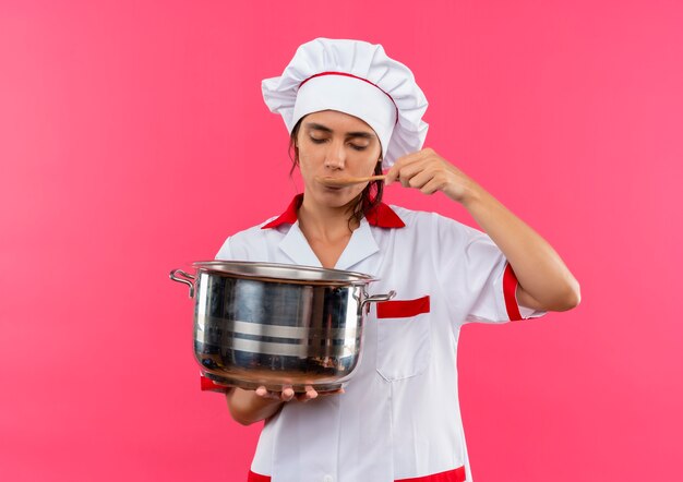 닫힌 된 눈으로 젊은 여성 요리사 요리사 유니폼을 입고 냄비를 들고 복사 공간으로 수프를 시도