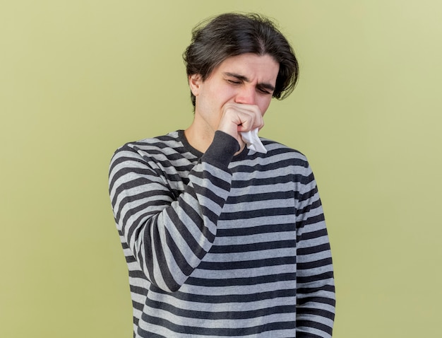 With closed eyes young ill man holding napkin putting hand on mouth isolated on olive green background