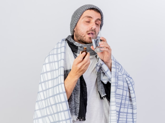 With closed eyes young ill man wearing winter hat and scarf wrapped in plaid isolated on white