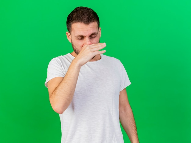 Бесплатное фото С закрытыми глазами молодой больной вытирает нос рукой, изолированной на зеленом фоне
