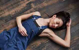 Free photo with eyes closed. girl in the blue uniform for the work is lying on wooden floor having relax