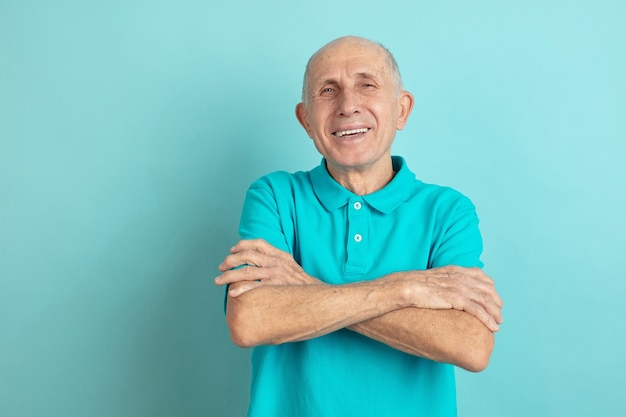 With hands crossed. Caucasian senior man's portrait isolated on blue studio background. Beautiful male emotional model. Concept of human emotions, facial expression, sales, wellbeing, ad. Copyspace.