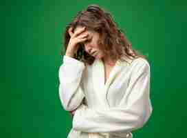 Free photo with lowered head unpleased young ill girl wearing white robe putting hand on forehead isolated on green