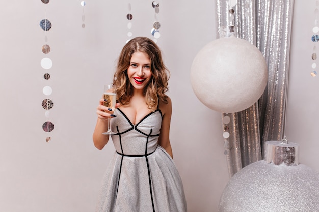 woman 25 years in beautiful bright dress with glass of champagne in hands, having fun on eve of Christmas holidays