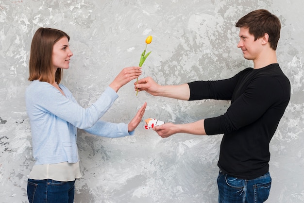 Woman accepting yellow tulip flower and no to cigarette packet offering by handsome man