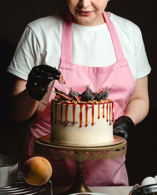 Woman adding fig piece on classic cake decorated with figs and syrup