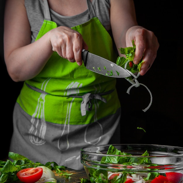 Woman adding spinach with sliced onion into seasonal salad side view