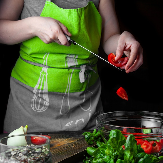 Женщина добавляет помидоры в салат с огурцами и шпинатом