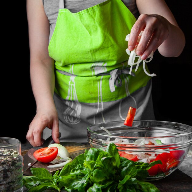 Woman adding vegetables into salad side view.