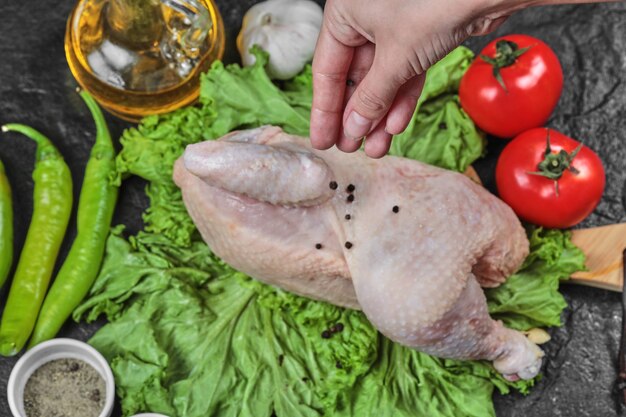 Woman adds spices to raw chicken with bunch of vegetables.